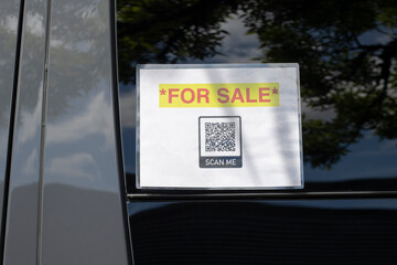 Closeup of the For Sale signage with a QR code for a website link posted on the window of a used vehicle.