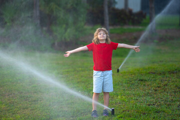 Obraz na płótnie Canvas Cute little kid watering grass in the garden at summer day. Child play in summer backyard. Cute little boy is laughing and having fun running under water spraying sprinkler irrigation. Watering grass.