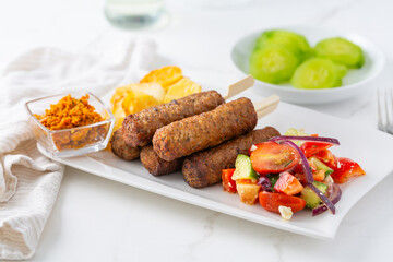 Traditional south european skinless sausages cevapcici made of ground meat with baked potatoes and small salad and dip