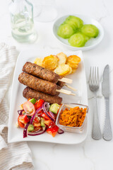 Traditional south european skinless sausages cevapcici made of ground meat with baked potatoes and small salad and dip