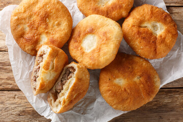 Traditional Peremech or belyash pies from yeast dough with grounded meat closeup on the paper on wooden table. Horizontal top view from above