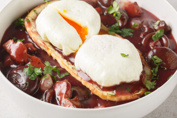 Oeufs en meurette Poached eggs in a red wine sauce with pearl onions, mushrooms and bacon closeup on the plate on the table. Horizontal