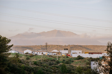 Sotogrande, Spain - January, 21, 2024 -  Rural landscape at dusk with a mountain backdrop, foreground showing buildings and power lines.