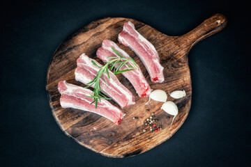 Top view of raw ribs with a rosemary and spices on a round wooden cutting board.
