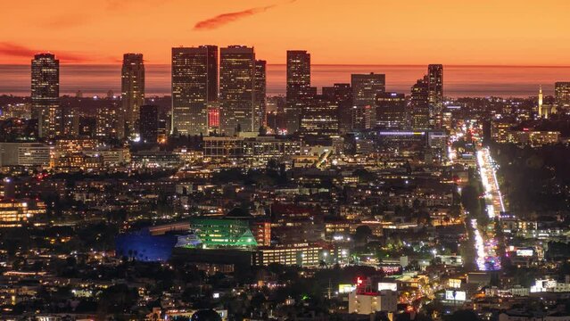 City of Los Angeles skyline at dusk, featuring illuminated Santa Monica Boulevard leading to Century City and Pacific Ocean on the horizon. Aerial view from Hollywood Hills at night.