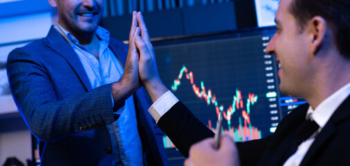 Cheerful two stock exchange traders giving high five for digital currency achievement on dynamic...