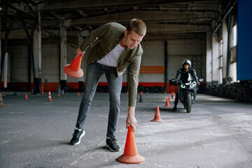 Motorbike driving school lesson with instructor putting cone on track