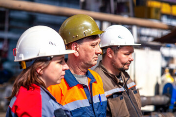 Professional team and portrait of an engineer standing in a group of out-of-focus workers at an industrial manufacturing factory. They workat at metallurgical or oil refinery plant.Inspection check.