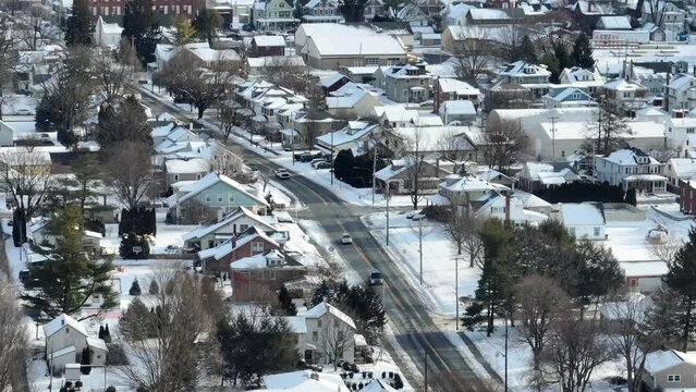 Christmas snow during holiday season in USA. Small town America after fresh winter snowfall. Cars pass by colorful homes lining street. Aerial drone view.