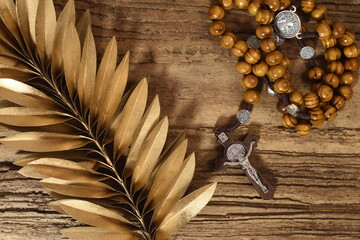 Rosary and golden palm leaf on wooden table. Palm Sunday 