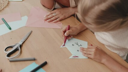 Slow motion shot of preteen girl drawing cats face with marker pens on origami figure and showing it to her mother