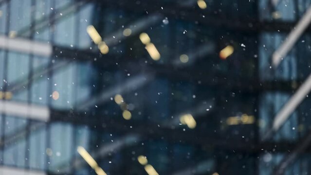 Snow falling against the background of the glass facade of a skyscraper in slow motion video. Large and small snowflakes falling against the background of an office building in the business district