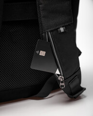 A bank card sticks out of a special card pocket on the strap of a black backpack