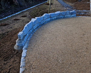 circular rest stop with an obelisk at the end of path in the park. bounded by stone wall in an arch along edge of the area. stones border tree which is protected against damage from impact, dog urine 
