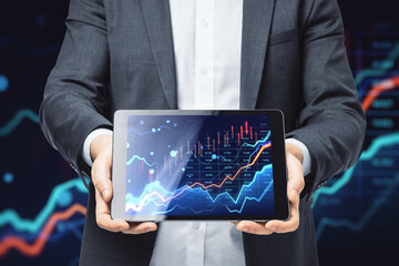 Close up of male hands holding tablet with glowing forex chart on blurry dark background. Trade, finance and market concept.