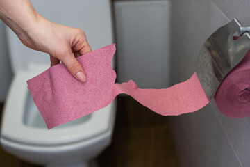 A female hand, woman holding a roll of pink toilet paper, digestive problems and defecation...
