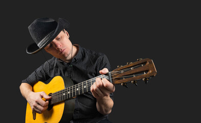 Man plays an acoustic guitar on a dark isolated background. A musician in a cowboy hat clamps the...