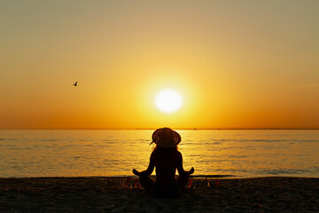 Young woman on tropical beach doing yoga meditating in lotus position at sunset. Serenity and yoga,...