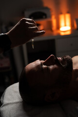 Oil is dripped onto a man's forehead for massage. Close up of a handsome man enjoying facial...