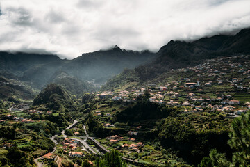 Scenic view of Madeira nestled amidst lush trees and clouds, set against a majestic valley.
