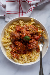 Meatballs with pasta and tomato sauce on plate on light kitchen background