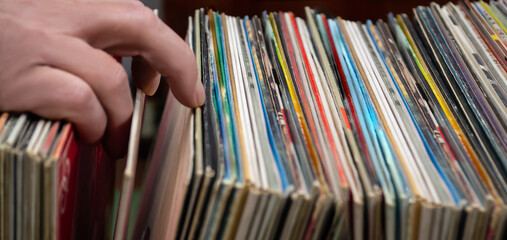 Close up of the hand of a man looking at vinyl records in a music shop.