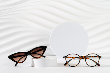 Classic tortoiseshell frame eyeglasses and trendy cat eye frame sunglasses on podiums on white...