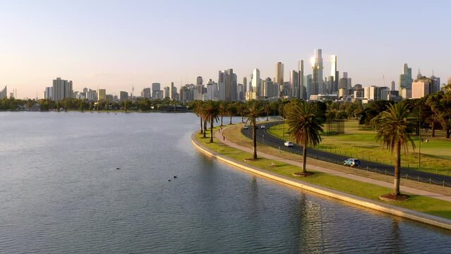 Aerial: Australia Melbourne City Center in Background Evening Golden Hour Flight over Beautiful Albert Park Lake