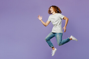 Full body side profile view fun young man he wears grey striped t-shirt casual clothes jump high run fast hurry up isolated on plain pastel light purple background studio portrait. Lifestyle concept.