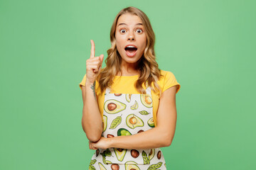 Young overjoyed housewife housekeeper chef cook baker woman wear apron yellow t-shirt point index finger up with new great idea isolated on plain pastel green background studio. Cooking food concept.