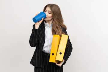 A young woman drinks her morning coffee and holds yellow folders with documents. Business woman in a business suit