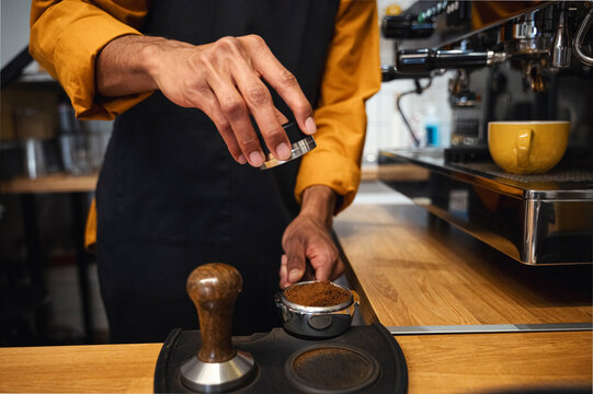 Barista tamping ground coffee in portafilter with tamper at cafe