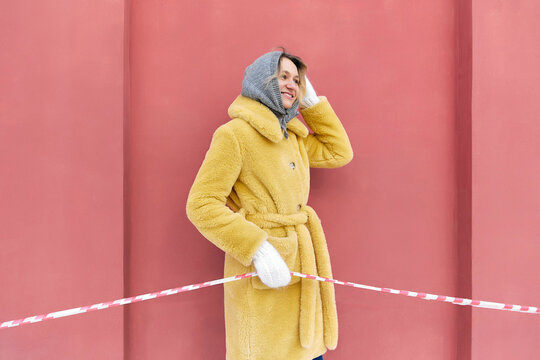 Happy young woman holding red and white barricade tape in front of peach wall