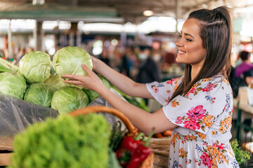 A photograph capturing a girl in a white dress at the market, carefully choosing a fresh cabbage...