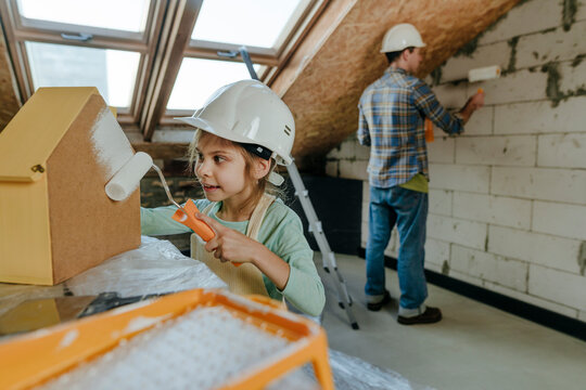 Girl wearing hardhat and helping father doing renovation work