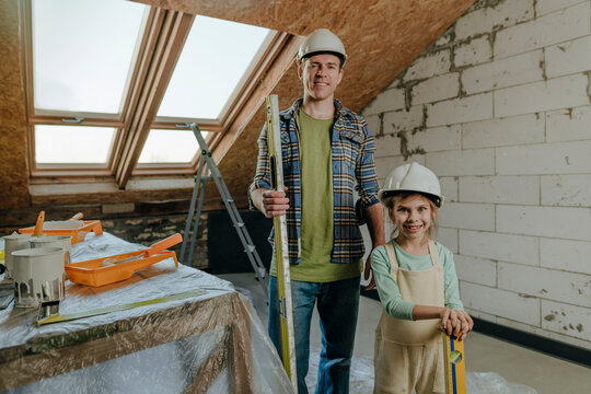 Man holding leveling tool and standing with daughter near table at home