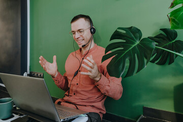 Smiling freelancer using headset and laptop for video call in front of green wall