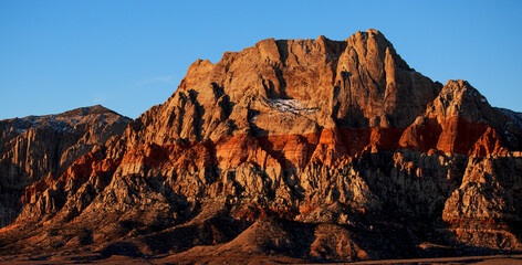 Lever de soleil sur Red Rock Mountain, Las Vegas, Nevada, États-Unis d'Amérique. Montagne à la roche rouge et jaune s'élevant au milieu d'une plaine désertique avec traces de neige sur la paroi. - obrazy, fototapety, plakaty