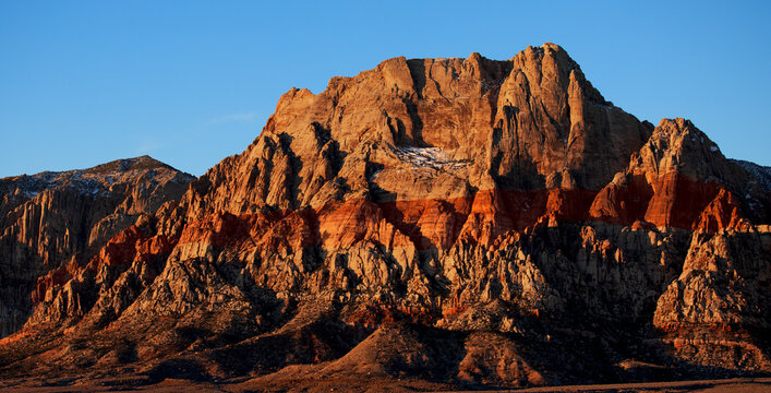 Lever de soleil sur Red Rock Mountain, Las Vegas, Nevada, États-Unis d'Amérique. Montagne à la roche rouge et jaune s'élevant au milieu d'une plaine désertique avec traces de neige sur la paroi.