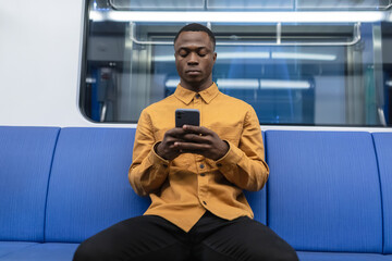 A stylish African-American man rides in a subway car. A man is sitting and holding a mobile phone...