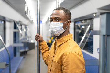 Fototapeta na wymiar Portrait of an African-American man in a protective mask who is riding in a subway car. A man looks at the camera
