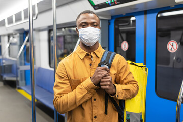 Portrait of a male courier in a protective mask on public transport. Food delivery during a pandemic