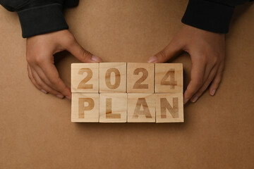 Hand arranging wooden cubes with 2024 PLAN text on brown background. Business plan concept