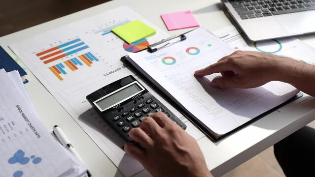 Asian male finance staff is calculating by using a calculator. Investment results to report to his boss at the meeting. On the table in the office, is the concept of calculating investment results.