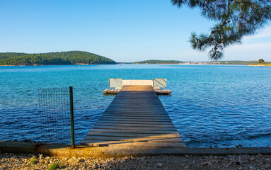 Obraz premium A swimming pier on the coast of Kasteja Forest Park - Park Suma Kasteja - in Medulin, Istria, Croatia. Premantura peninsula is in the background. December