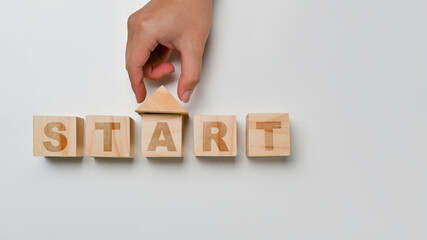Hand putting triangle block over wooden blocks with START word in the shape of a house. Business investment concept