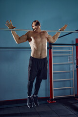 Shirtless athletic young man training in gym, doing pull ups exercises, building strong, muscular...