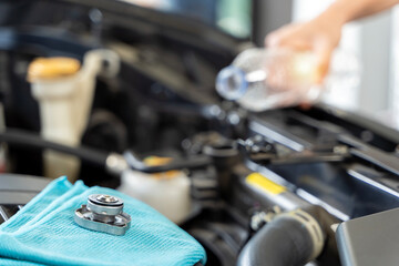 A woman takes matters into her own hands radiator refill. Mechanic performing car engine repair in...