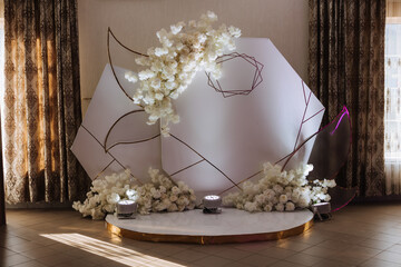 The photo zone at a wedding or birthday celebration is decorated with flowers and illuminated by artificial light
