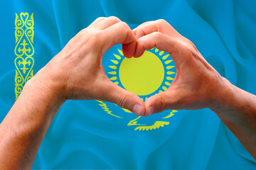 close-up of male hands in heart form against background of silk national flag of Kazakhstan,...
